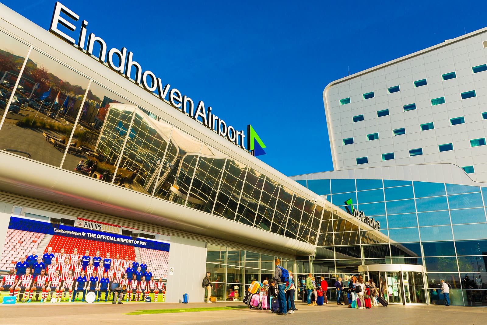 Reizigers met koffers voor de terminal van Eindhoven Airport
